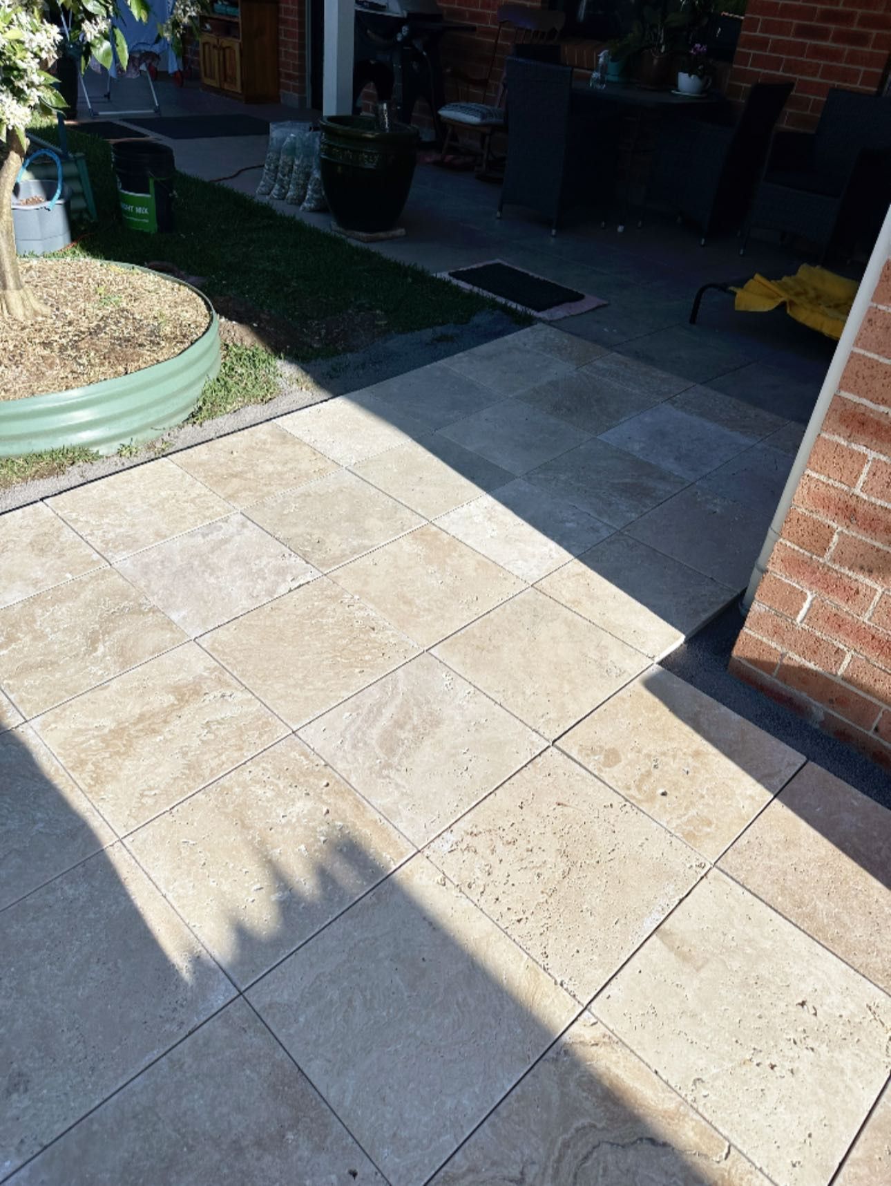 Beige stone patio with sunlight, brick wall on right, green lawn with a tree on left. — East Coast Paving in Seaham, NSW