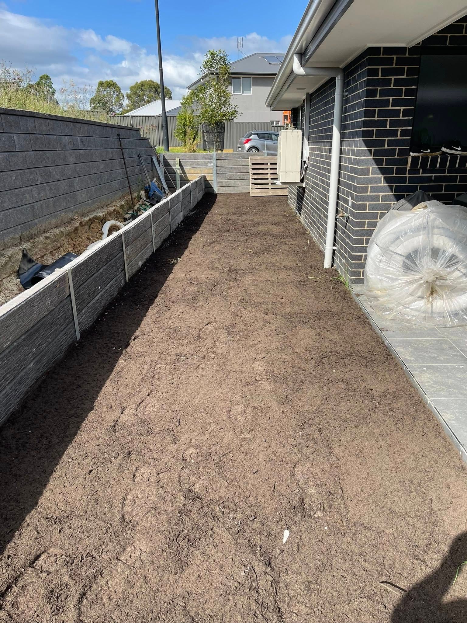 Narrow dirt pathway beside a house and retaining wall under a bright sky. — East Coast Paving in Seaham, NSW