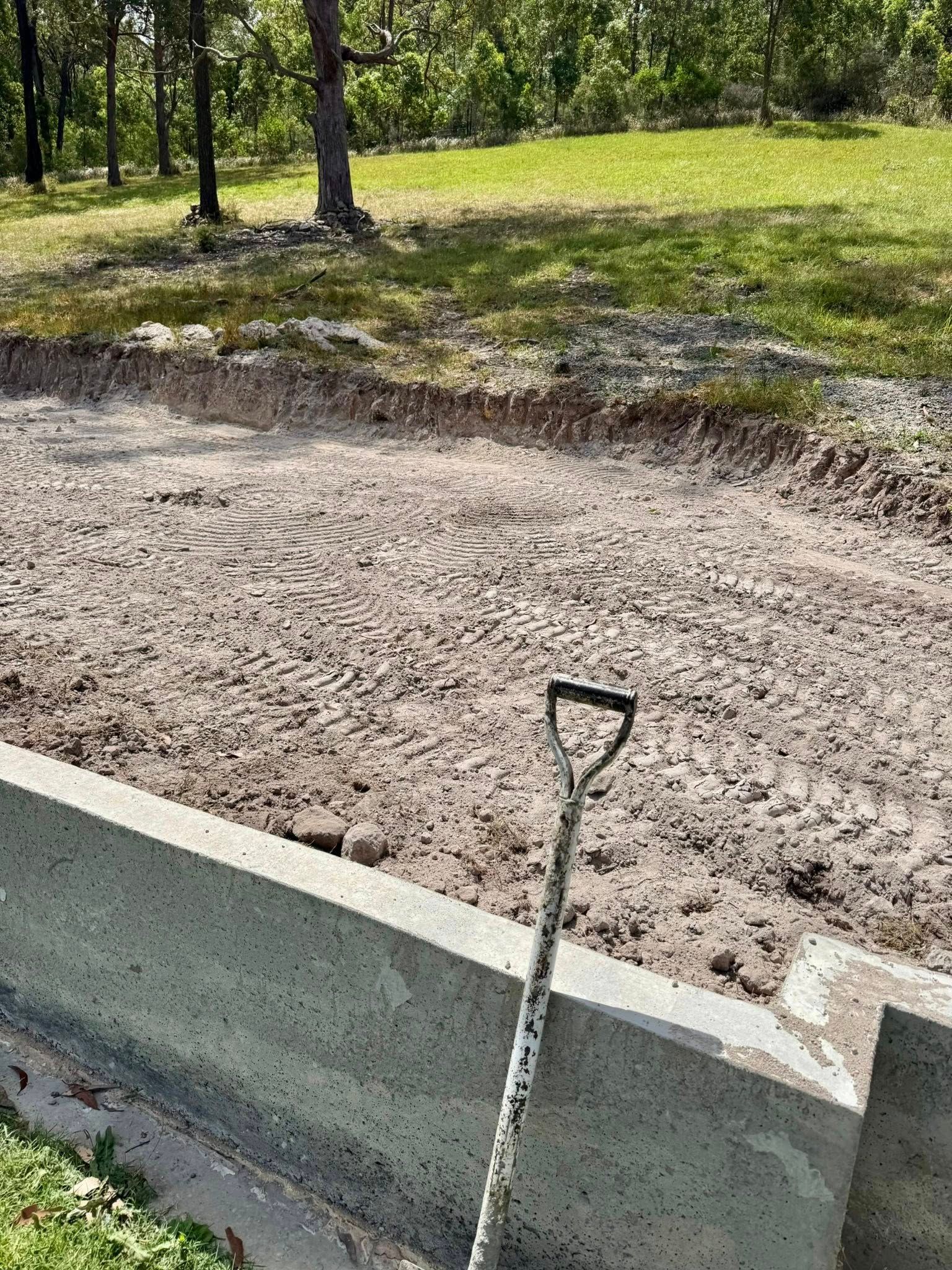Shovel rests on concrete steps near a dirt clearing, likely for a landscaping project, with trees and grass in the background. — East Coast Paving in Seaham, NSW