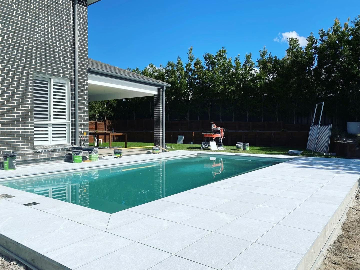 Excavator digging a trench in a grassy yard, trees in the background under a blue sky. — East Coast Paving in Seaham, NSW