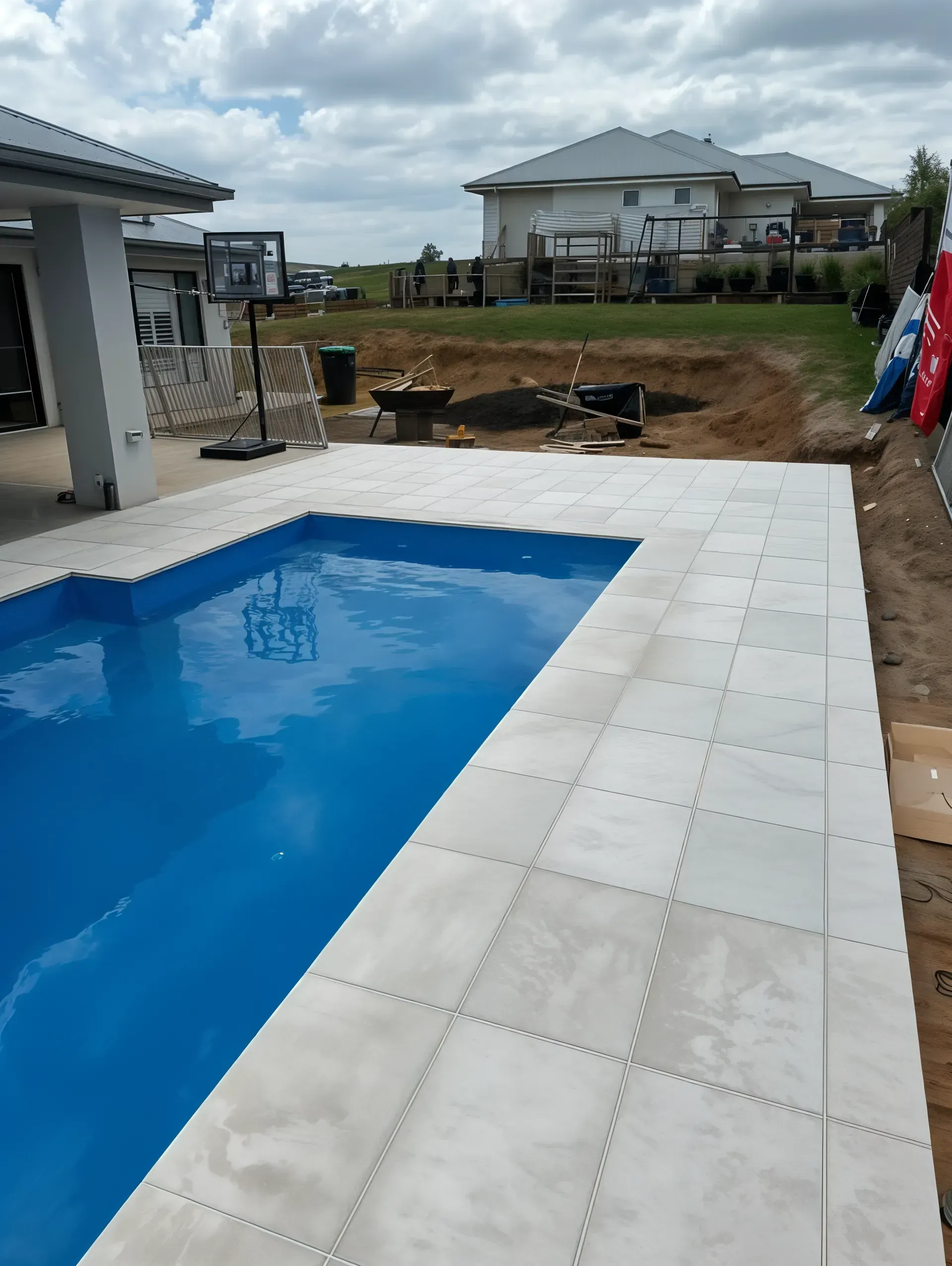 Swimming pool with light-colored tile surround; in the background, a house and construction. — East Coast Paving in Seaham, NSW