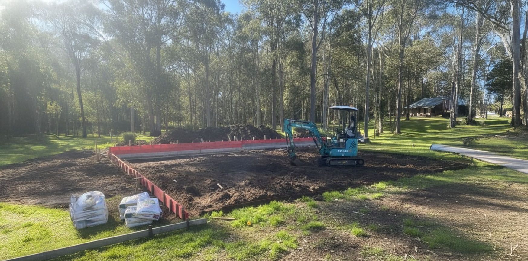 Construction site with a small excavator on a patch of dirt surrounded by trees.