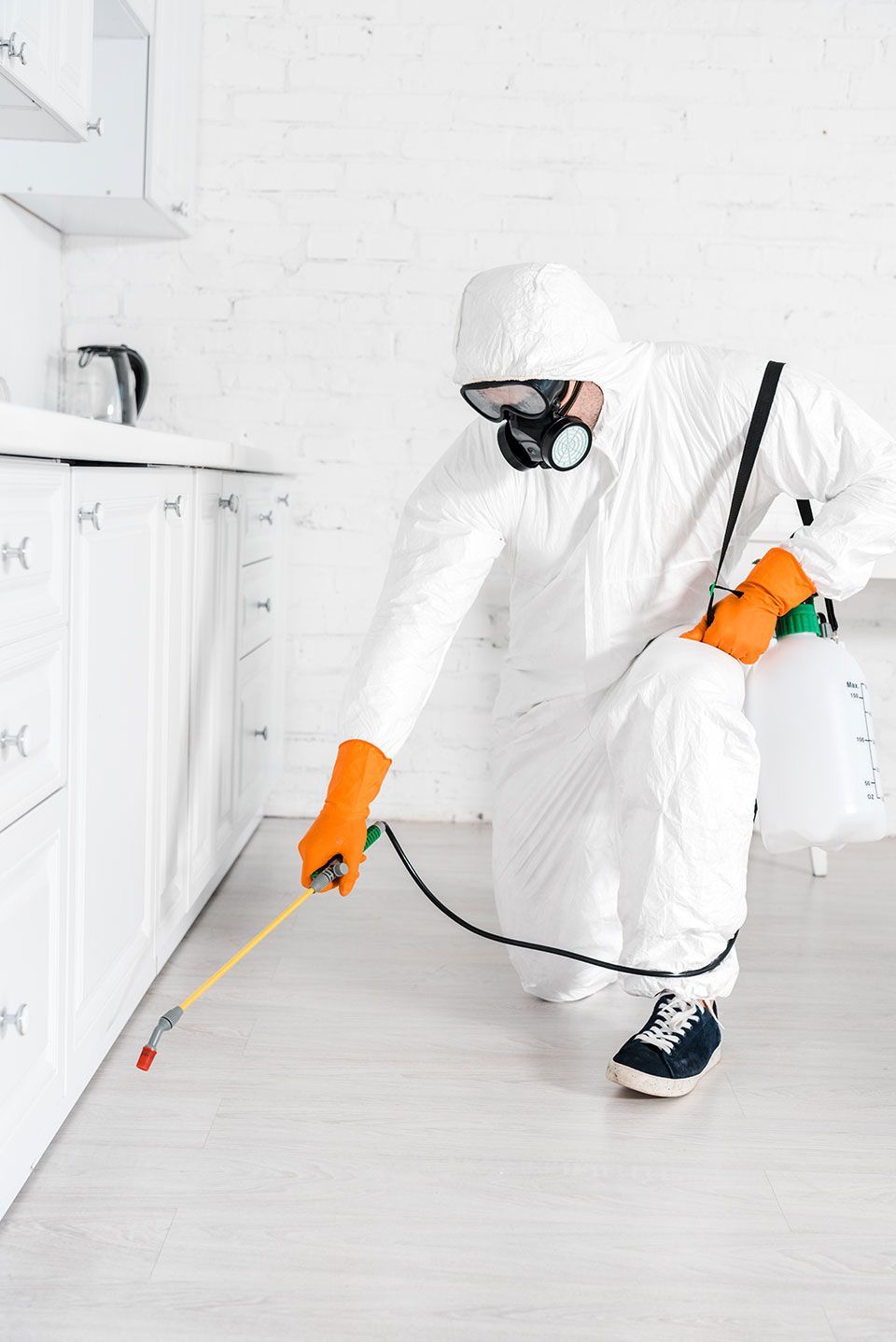 exterminator in protective mask using toxic spray near kitchen cabinet