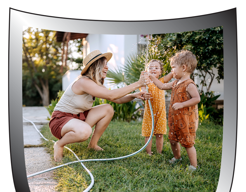 A woman and two children are playing with a hose in the grass.