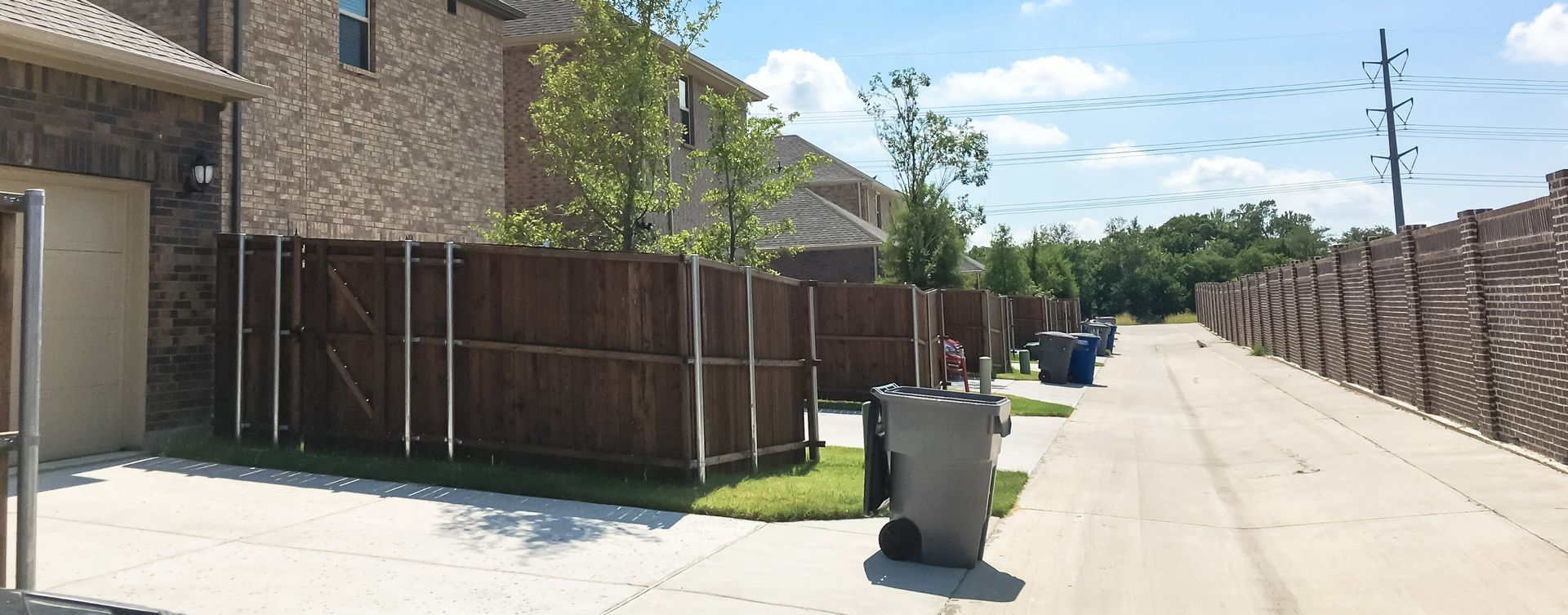 A row of houses with a wooden fence and trash cans on the side of the road.