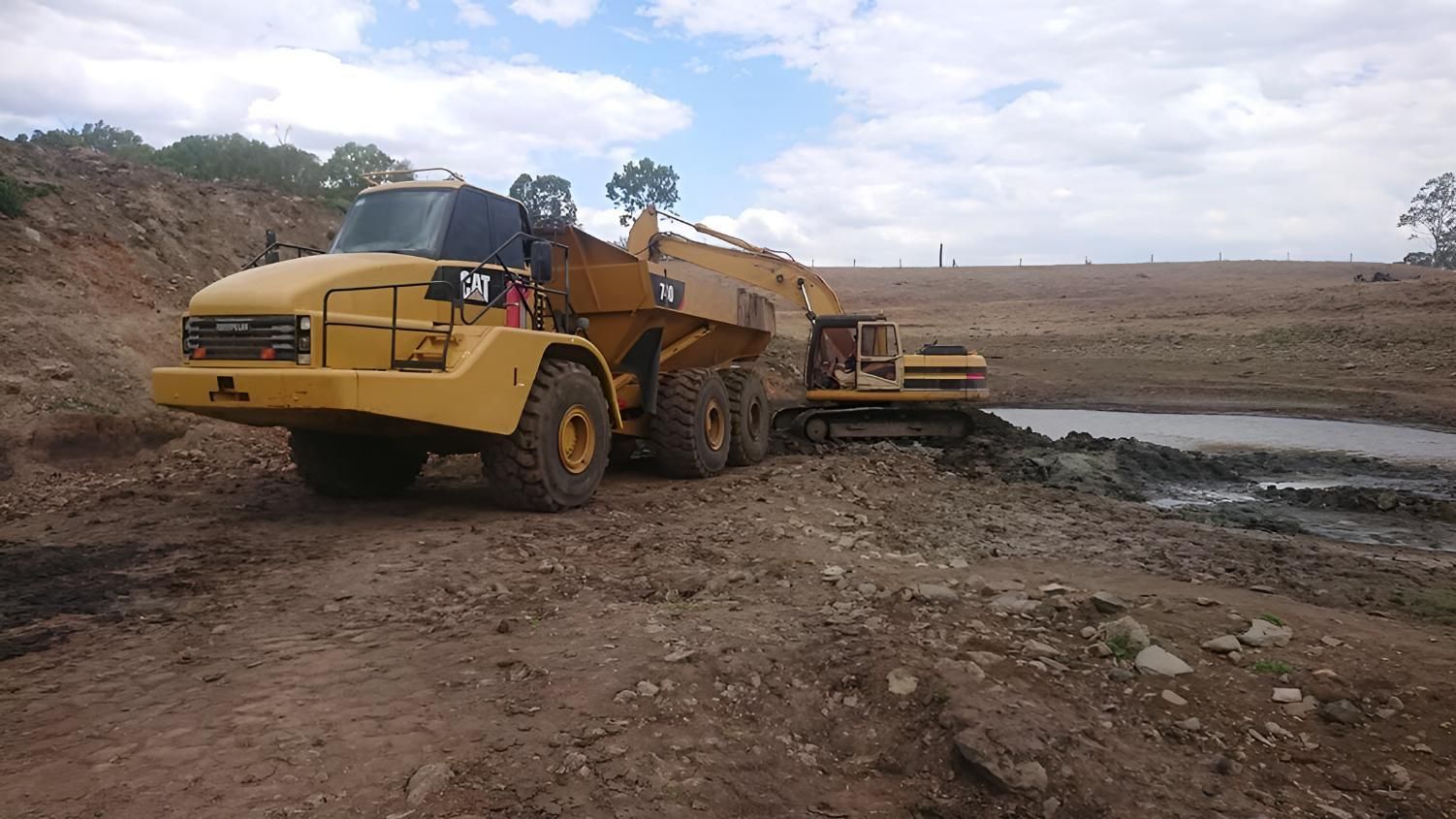 A Yellow Dump Truck Is Parked Next To A Bulldozer — Greenslade's Dozer & Excavator Hire Pty Ltd In Taabinga, QLD