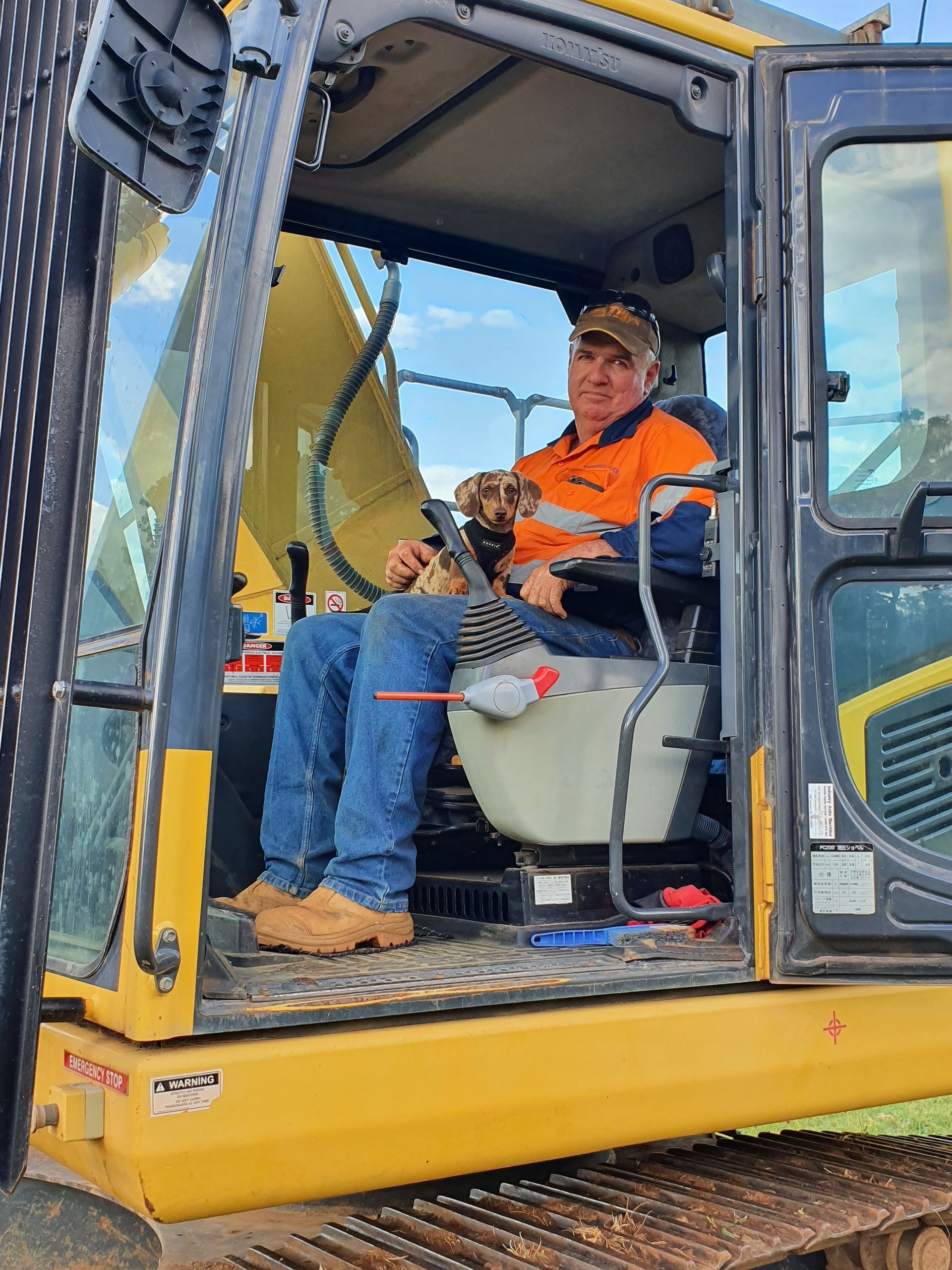 A Man Is Holding A Dog While Sitting On A Cat Bulldozer — Greenslade's Dozer & Excavator Hire Pty Ltd In Taabinga, QLD