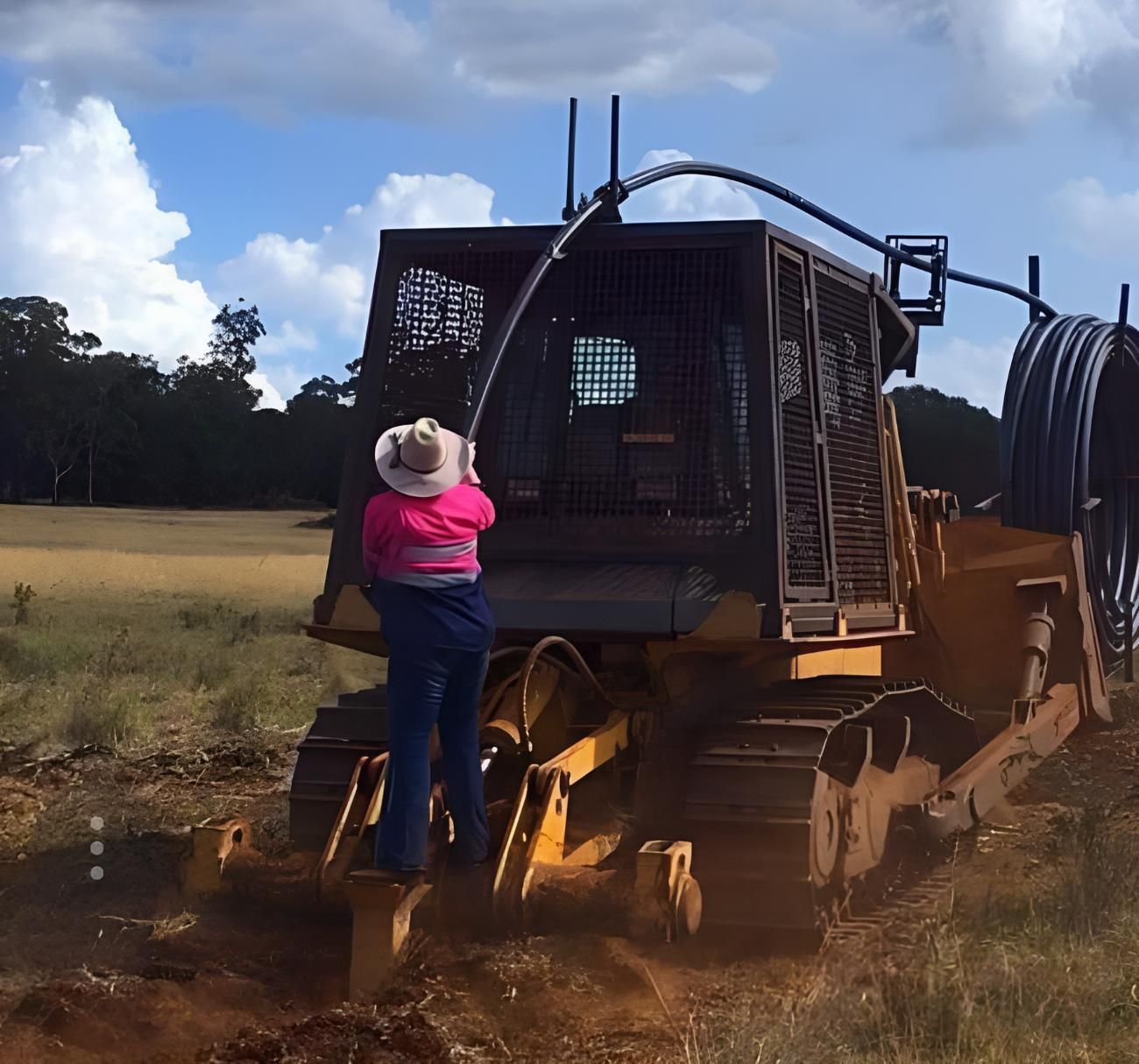 A Man Is Standing Next To A Bulldozer In A Field — Greenslade's Dozer & Excavator Hire Pty Ltd In Taabinga, QLD