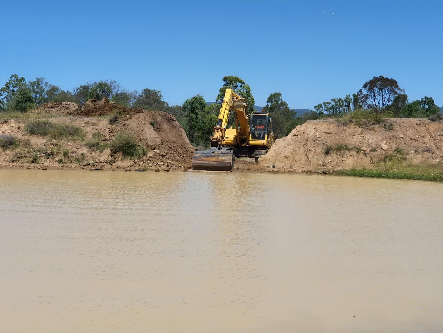 A Yellow Excavator Is Digging In A Dam — Greenslade's Dozer & Excavator Hire Pty Ltd In Taabinga, QLD