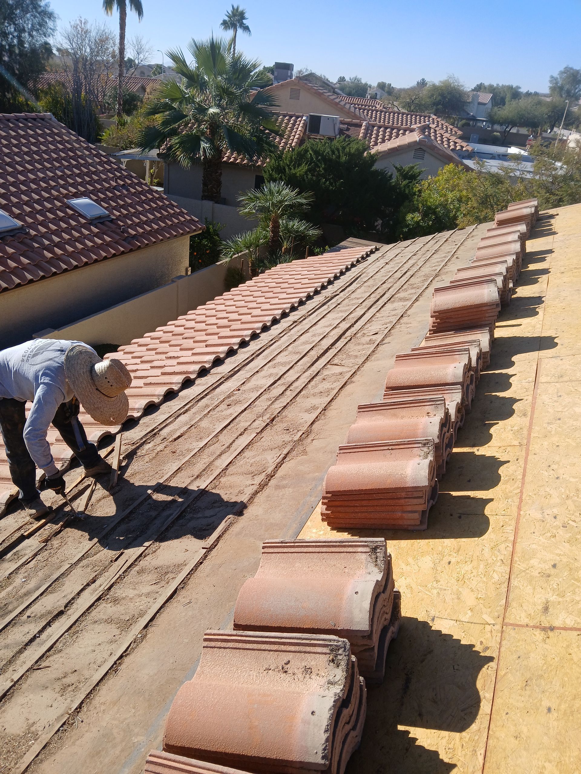 Roofer laying clay tiles on a roof; stacks of tiles, a sunny day.