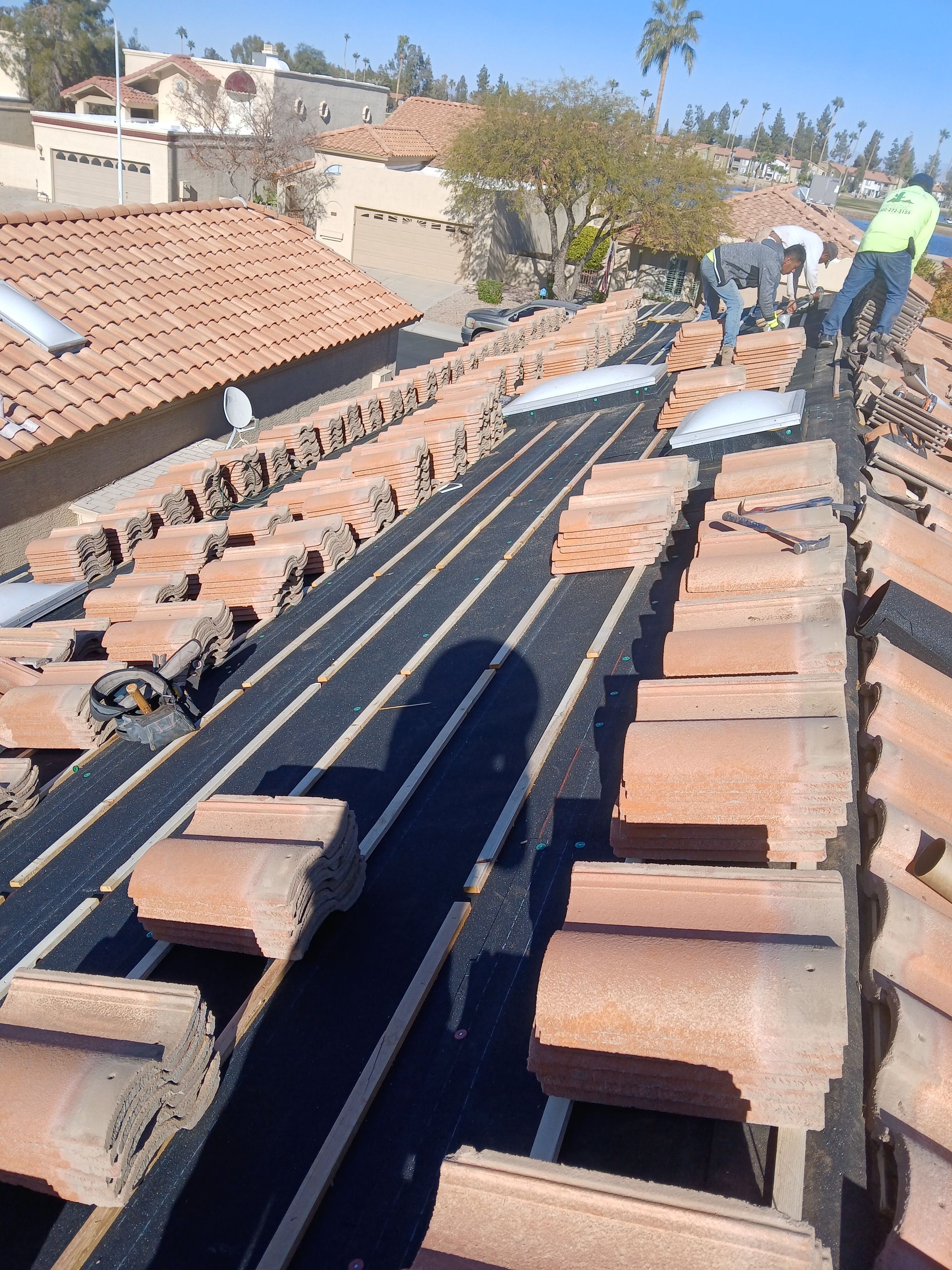 Roofers replacing clay tiles on a red-tiled roof; blue sky, sunny day.