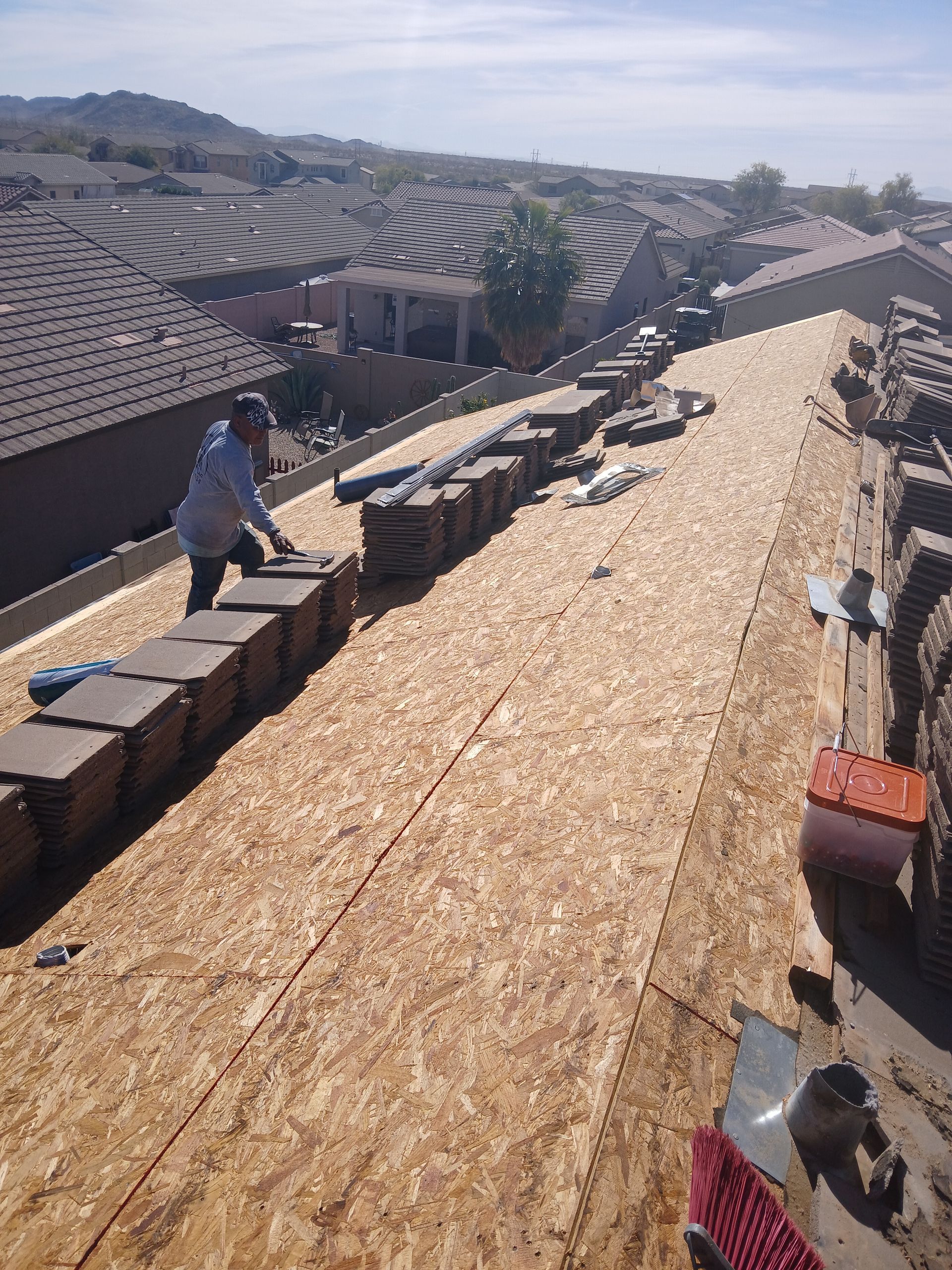 Roofer installing tiles on a residential roof, with bundles of tiles lined up; sunny day.