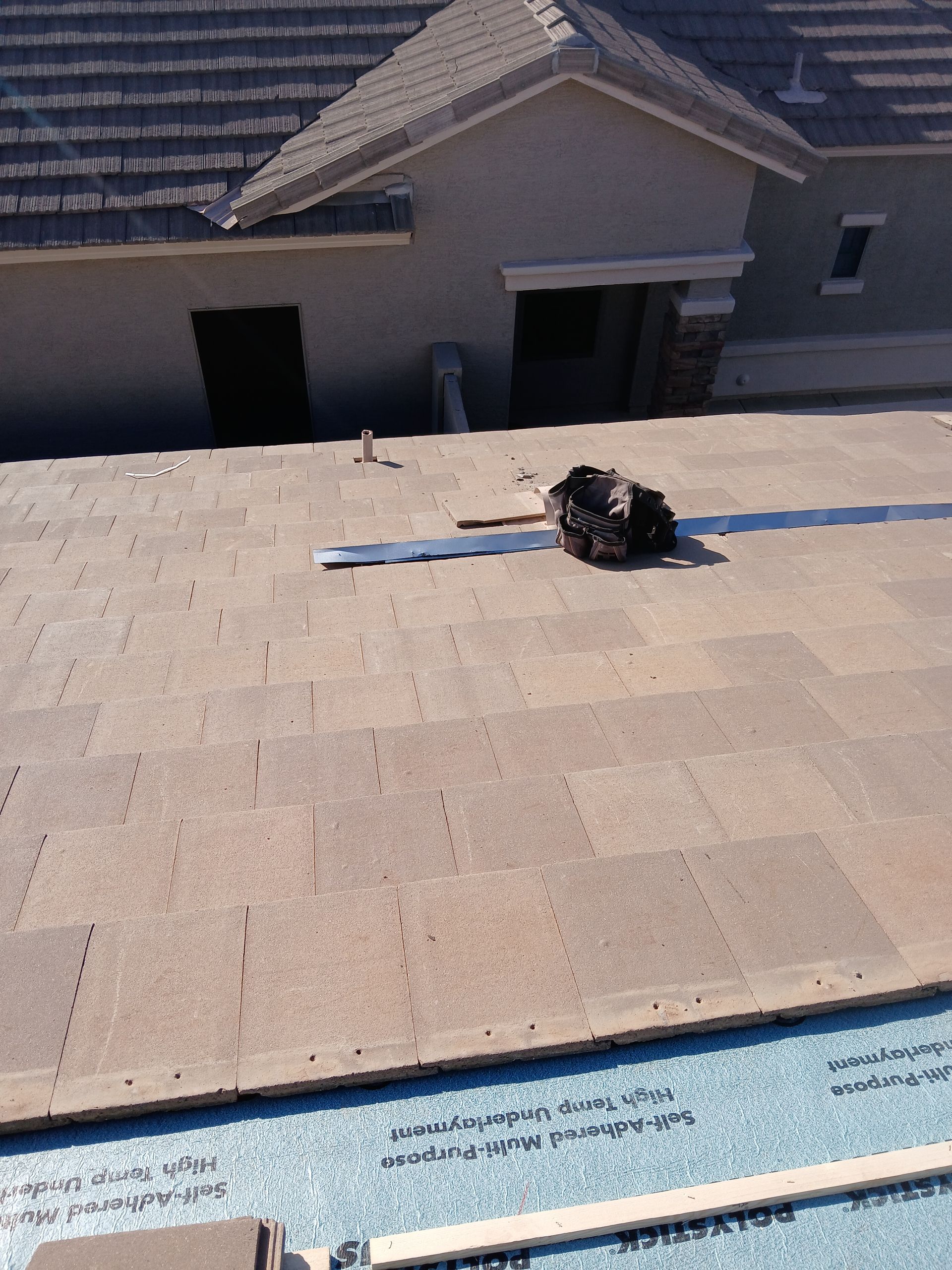 View from a rooftop shows partially installed brown roofing material and a house.