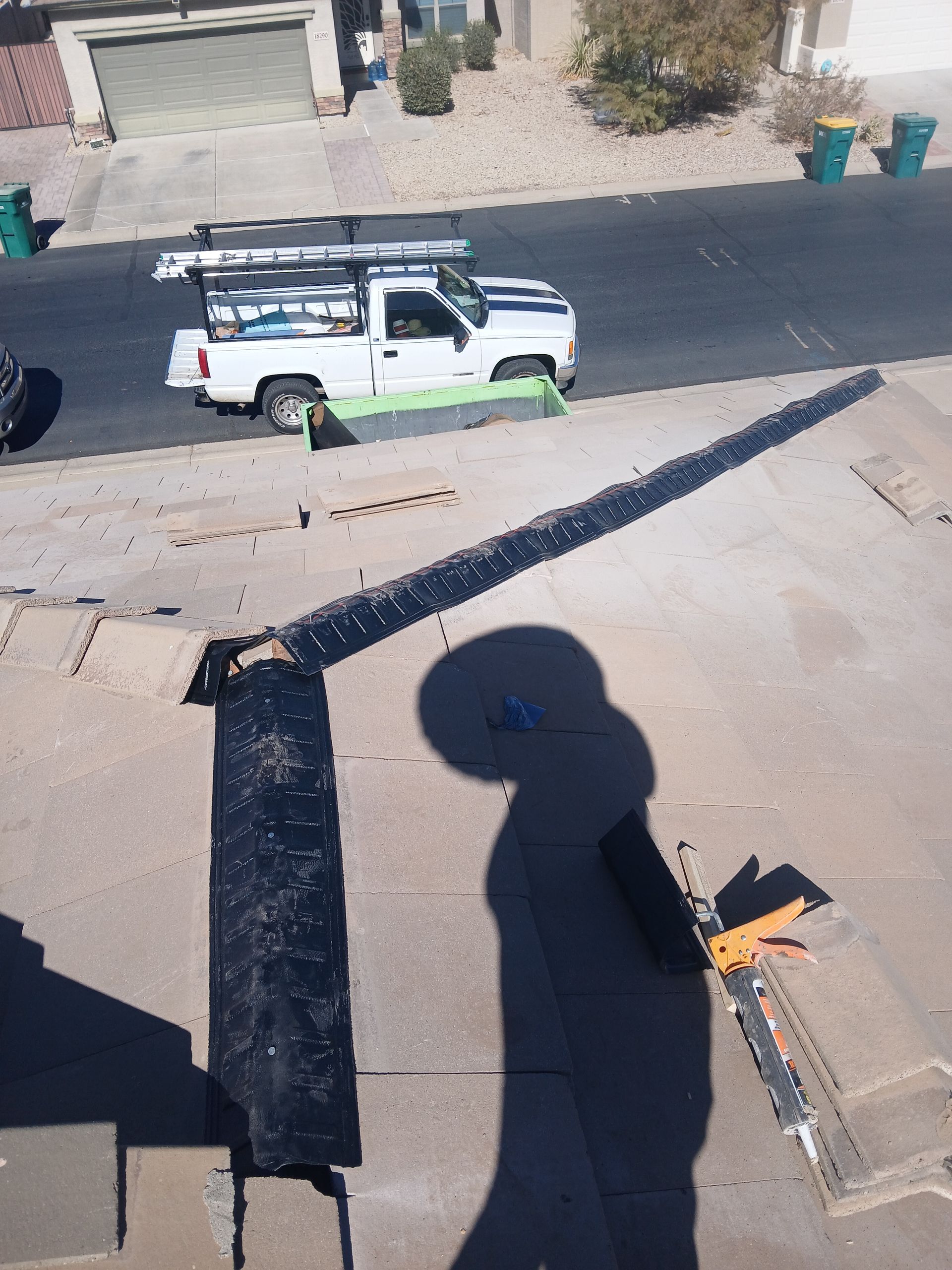 White truck parked near roof, shadow of person working on roof in sunny residential area.