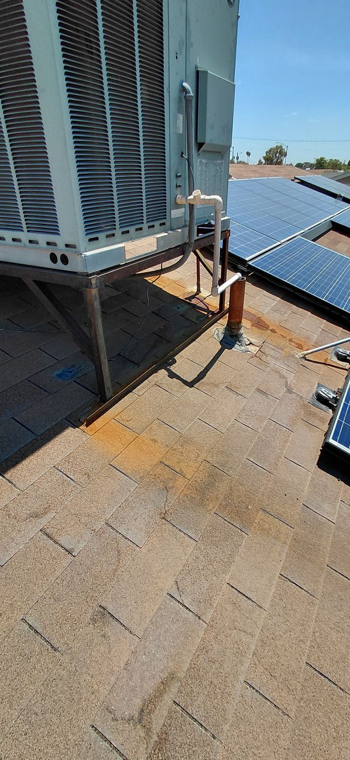 Rooftop view of an air conditioning unit with solar panels, and shingled roof.
