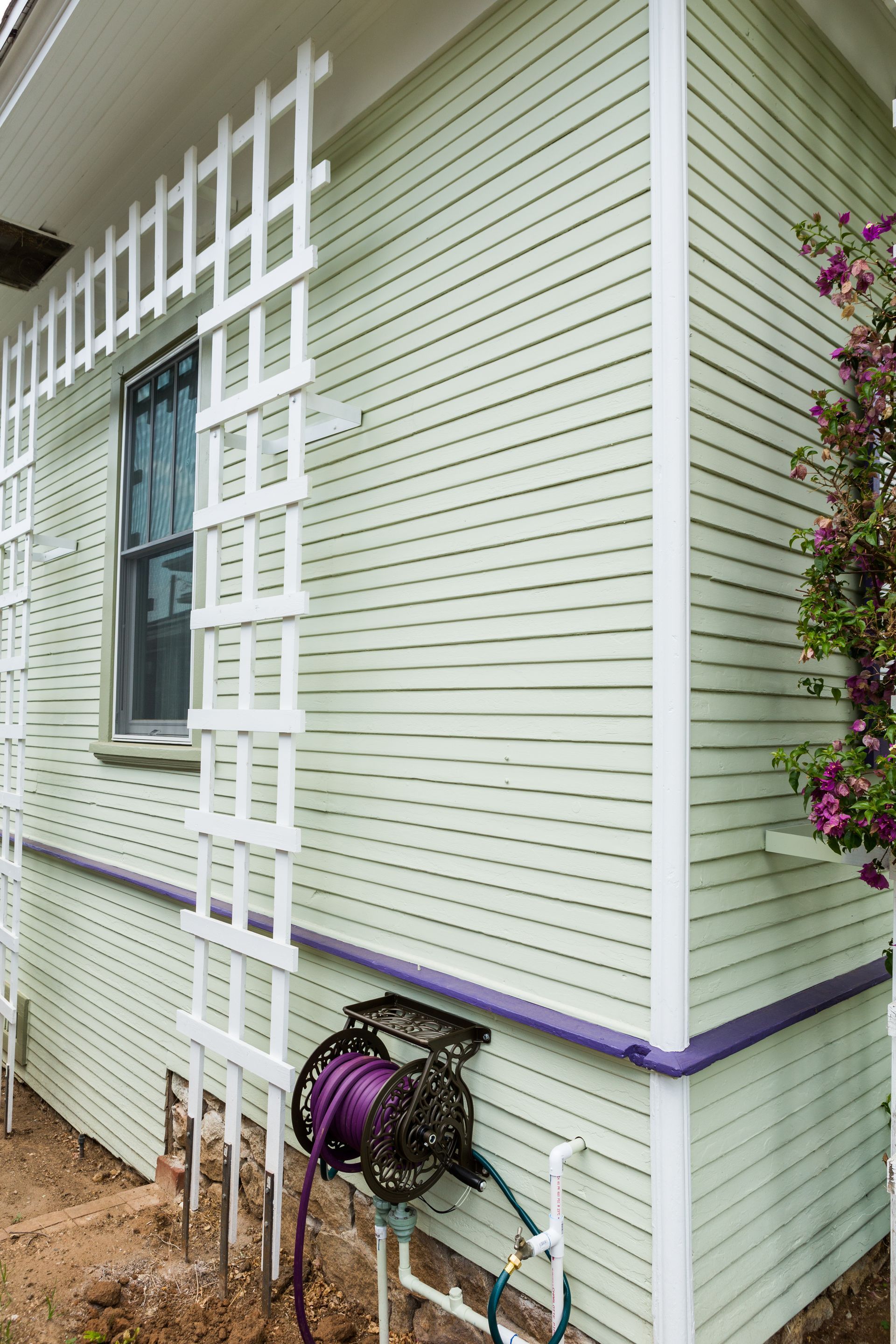 A green house with a white trellis and a hose reel on the side.
