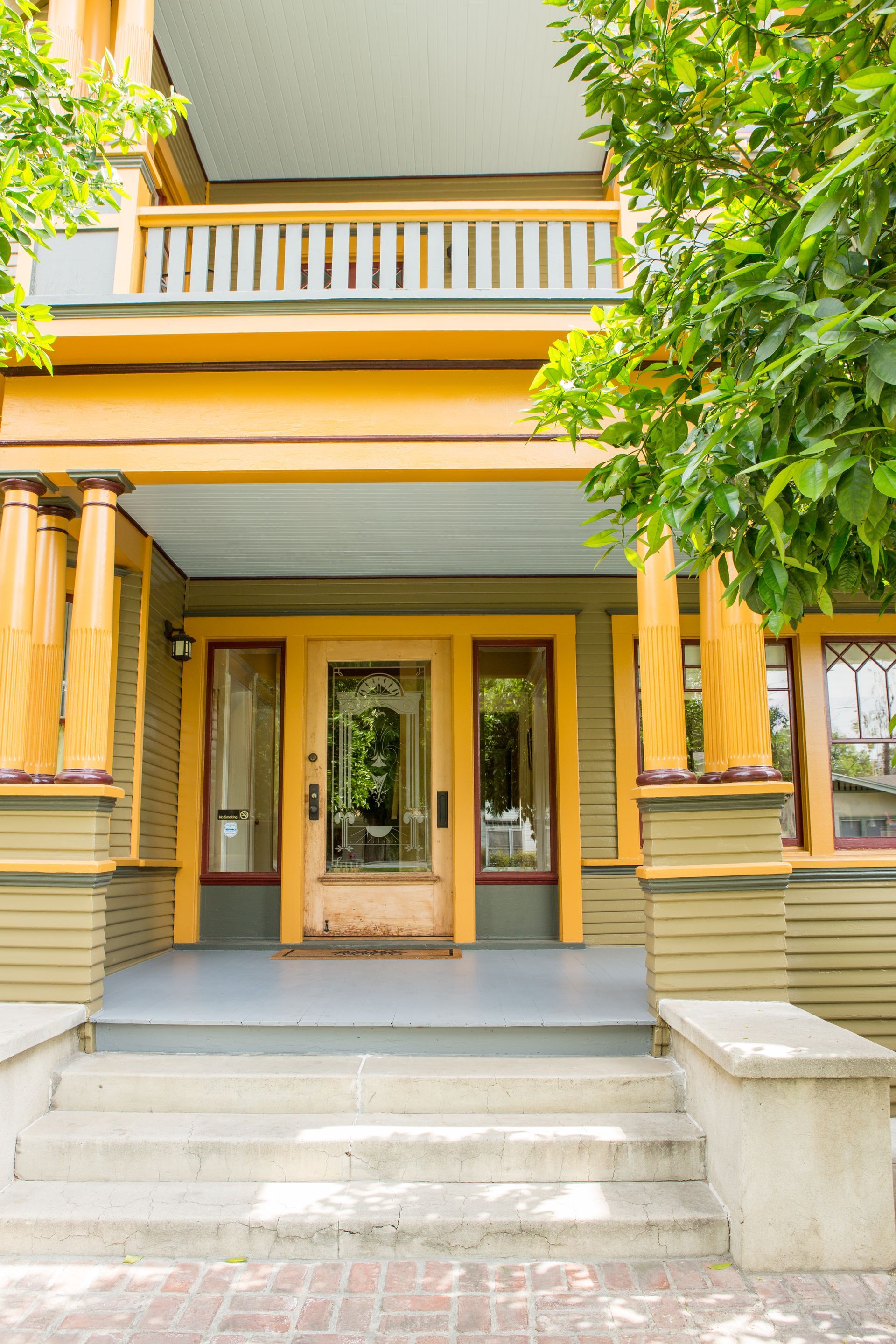 A yellow house with a porch and stairs is surrounded by trees.
