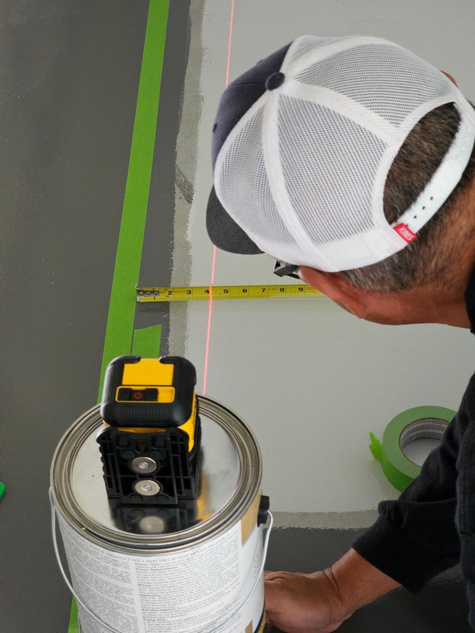 A man is measuring a can of paint with a tape measure