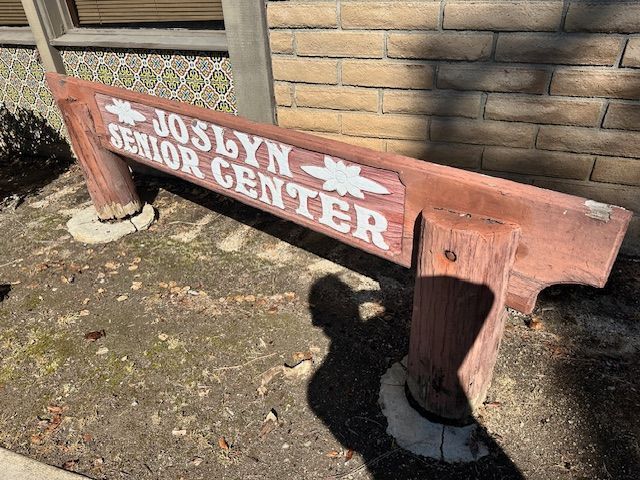 A wooden sign for joslyn senior center is sitting in front of a brick building.