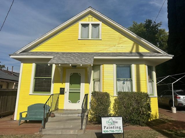 A yellow house with a green door and a sign that says painting