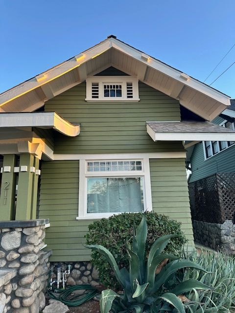A green house with a white window and a stone wall