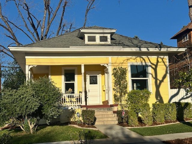 A yellow house with a porch and a gray roof