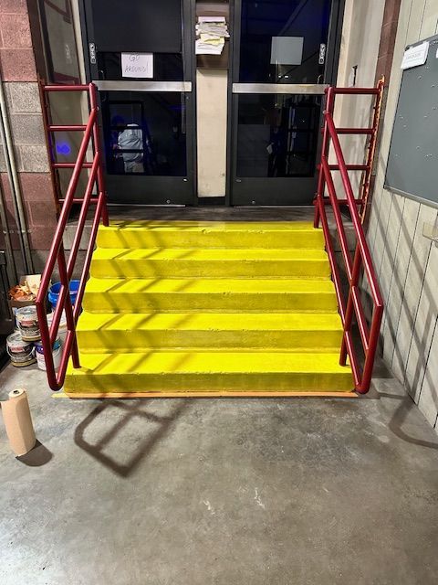 A set of yellow epoxy stairs with a red railing in front of a door.