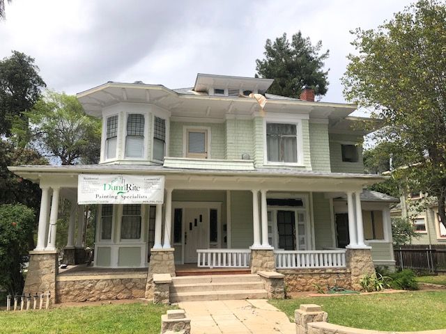 A large green house with a porch and a sign on the front of it.