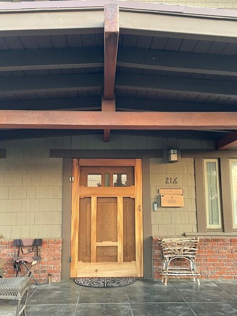 The front door of a brick house with a wooden door and a covered porch.