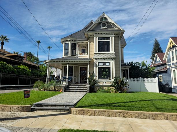 Fresh paint for A two-story Victorian house with light-colored siding, dark trim, a gabled roof, and a stone walkway leading to the porch.