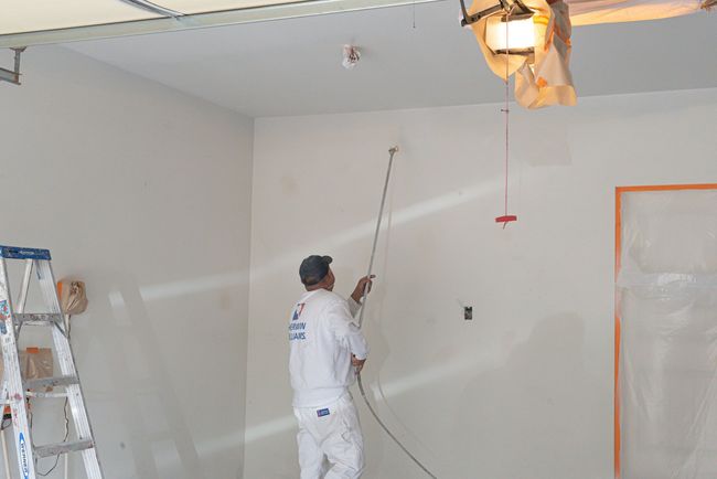 A man is spray painting a wall in a garage.
