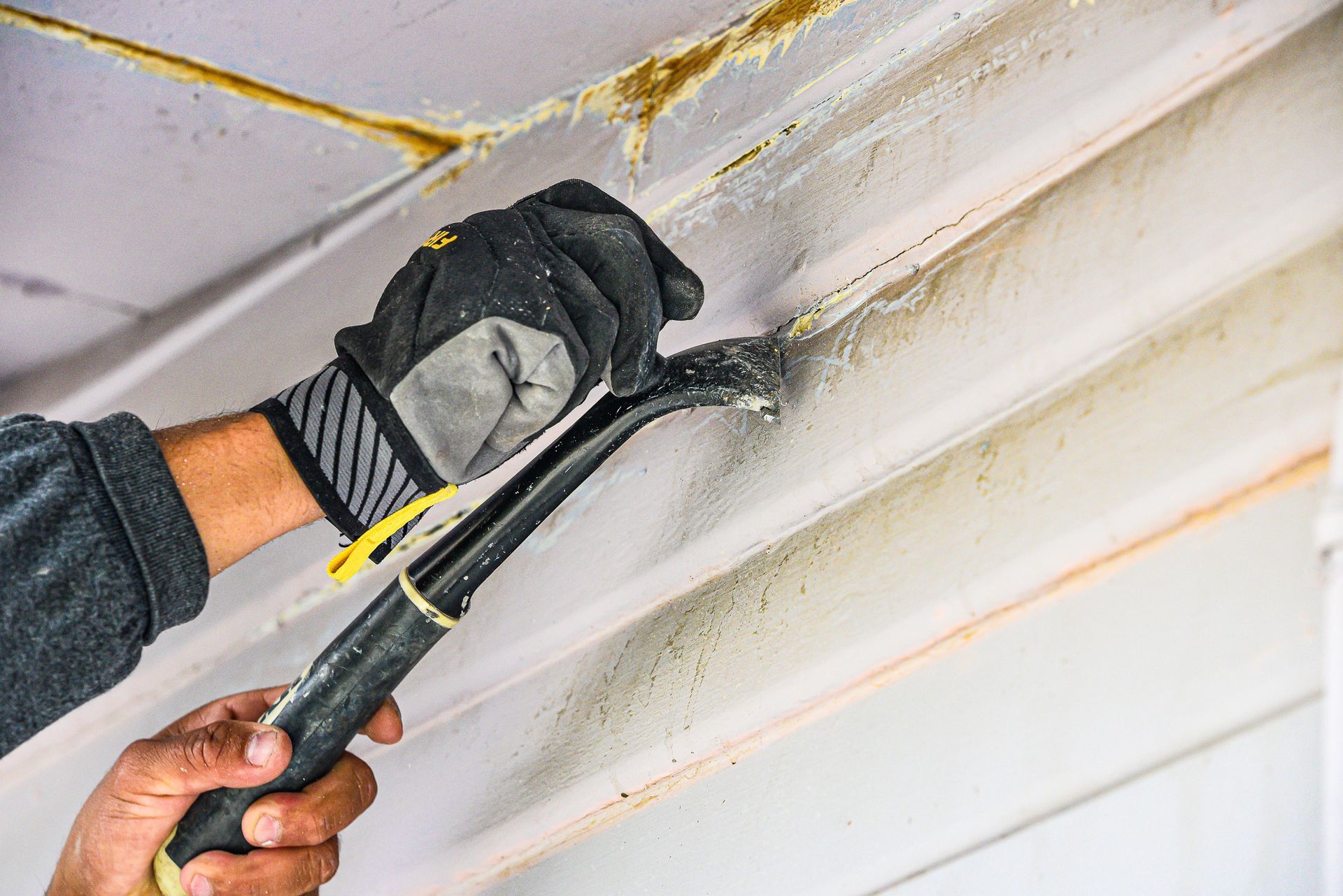 A person is using a hammer to remove mold from a ceiling.