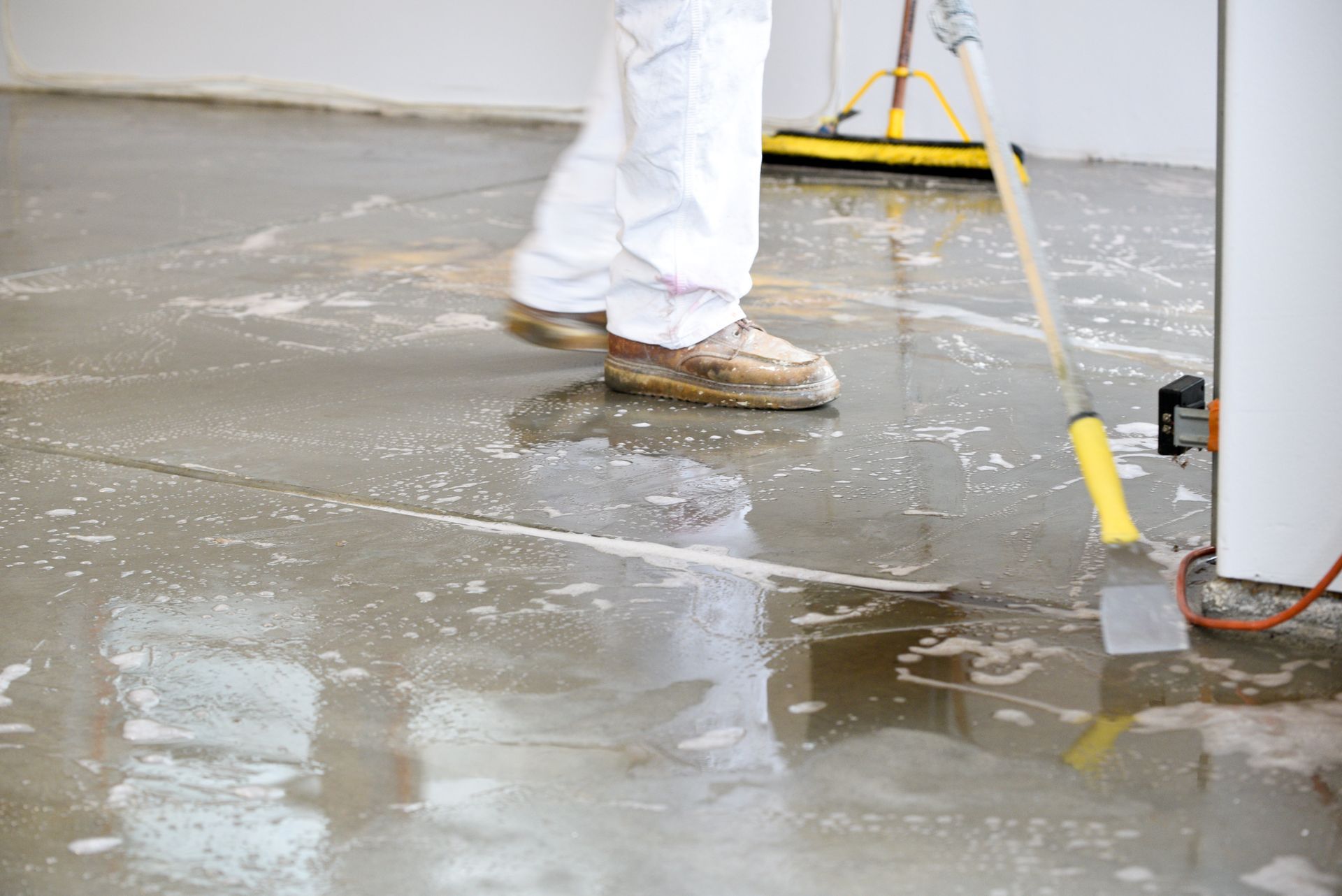 A person is cleaning a concrete floor with a broom. Etching concrete floor for epoxy in Redlands