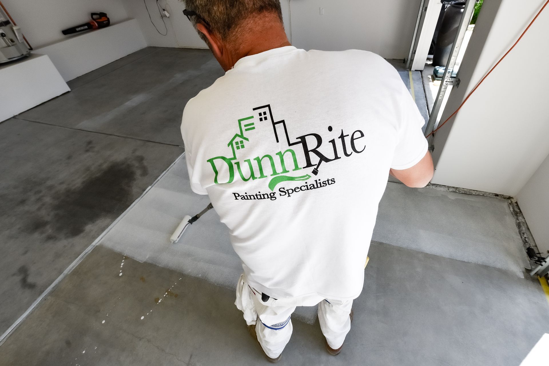 A man wearing a dunn rite shirt is painting a floor