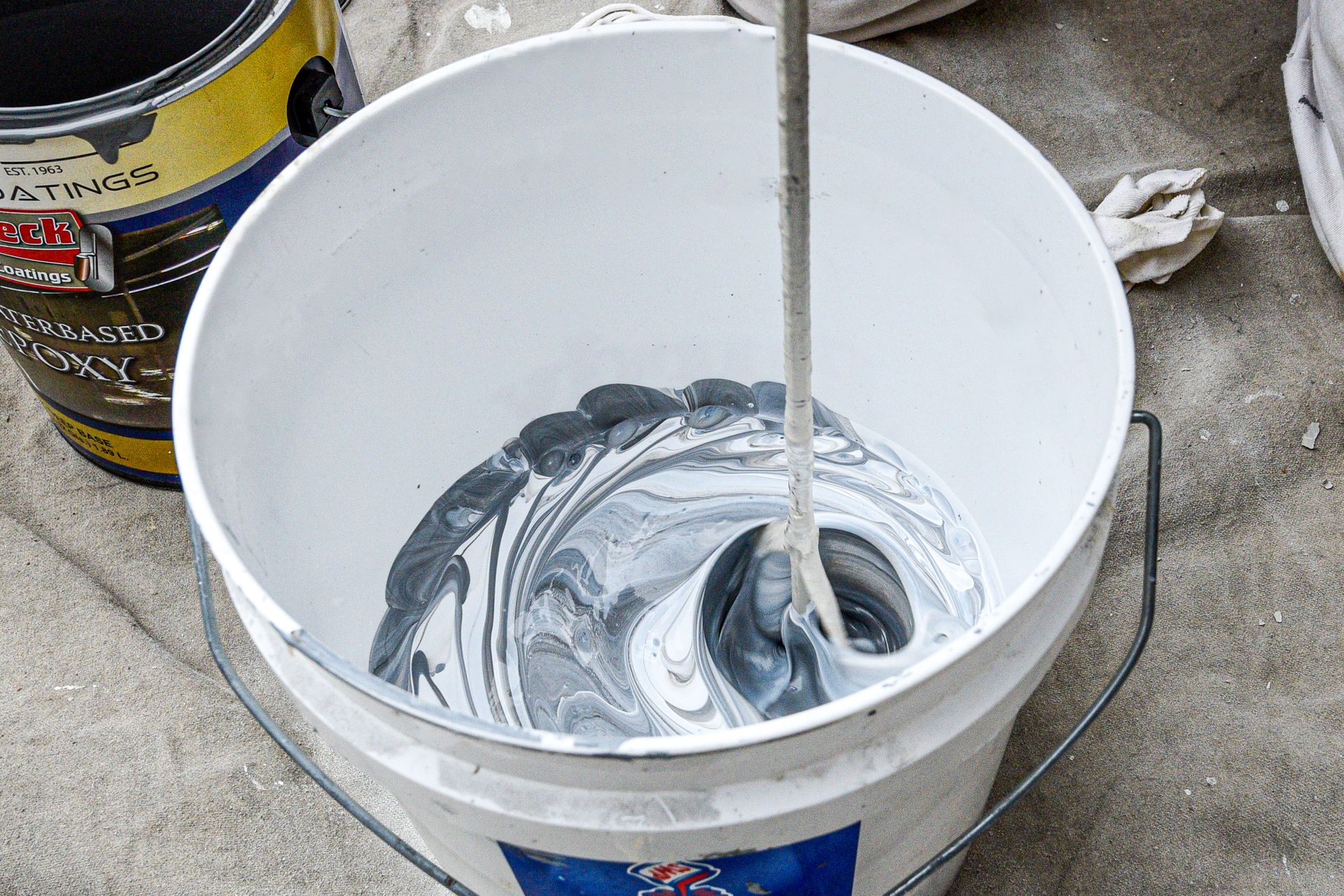 A man is measuring a can of epoxy paint with a tape measure