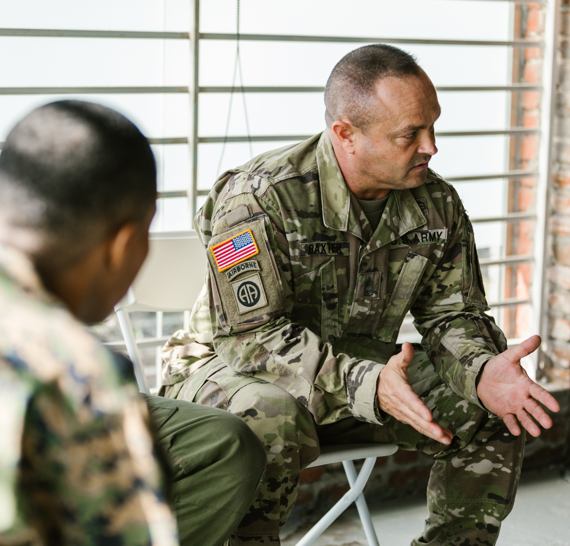 a man in a military uniform is sitting in a chair talking to another man .