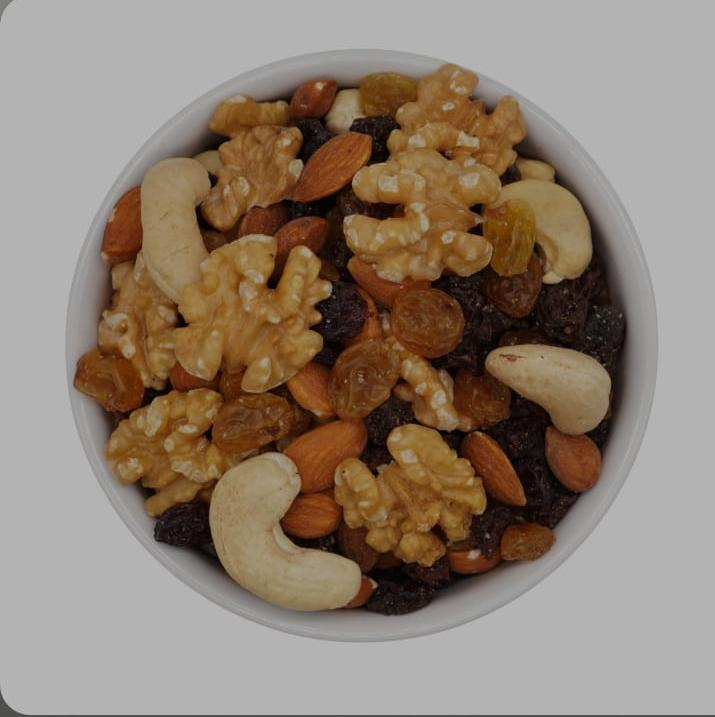 Cuenco de frutos secos mixtos, que incluyen nueces, anacardos, almendras y pasas, sobre un fondo gris.