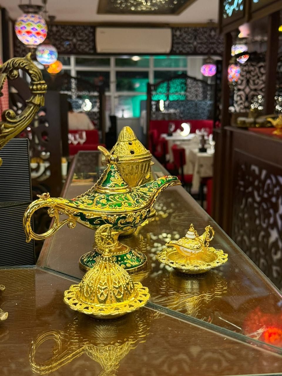 Tetera y pequeño cuenco dorados y ornamentados sobre la mesa de un restaurante, con coloridas luces colgantes al fondo.