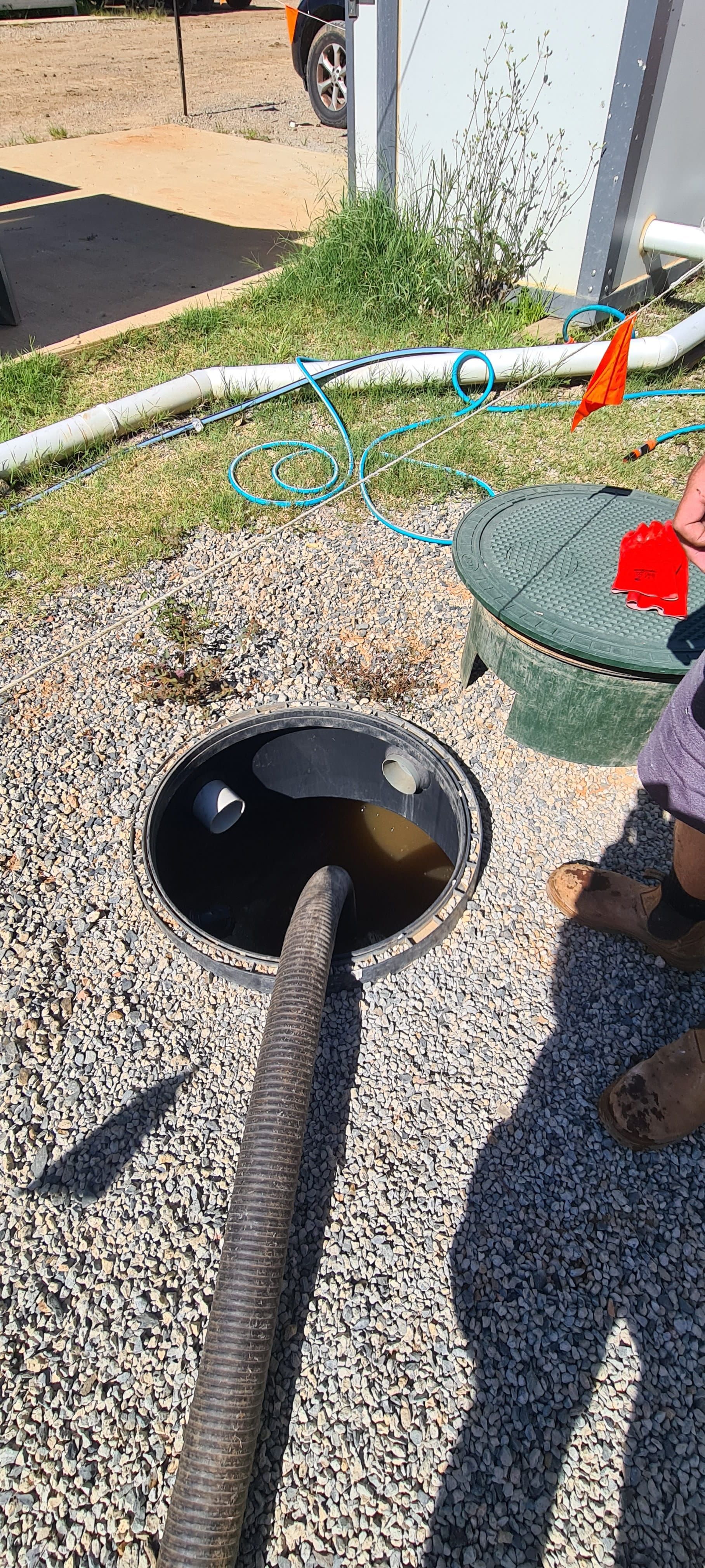Black liquid being pumped from a septic tank in a gravel yard
