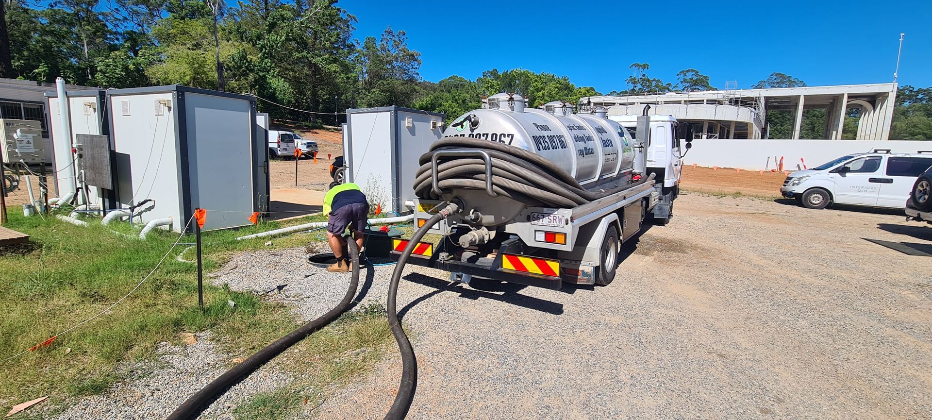 A sewage truck is parked next to containers and a worker connects hoses on a sunny day — Raptor Waste Management in Coolangatta, QLD