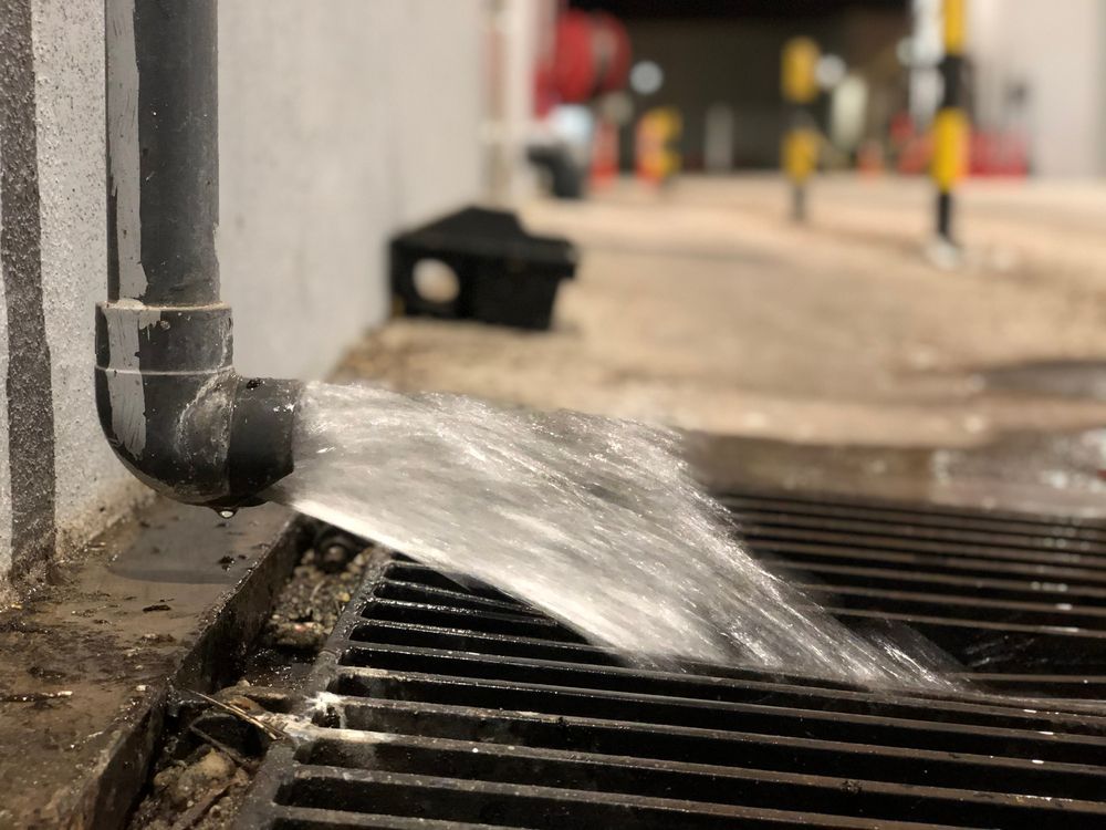 Water Spurting From a Black Pipe Into a Metal Grate — Raptor Waste Management In Ormeau, QLD
