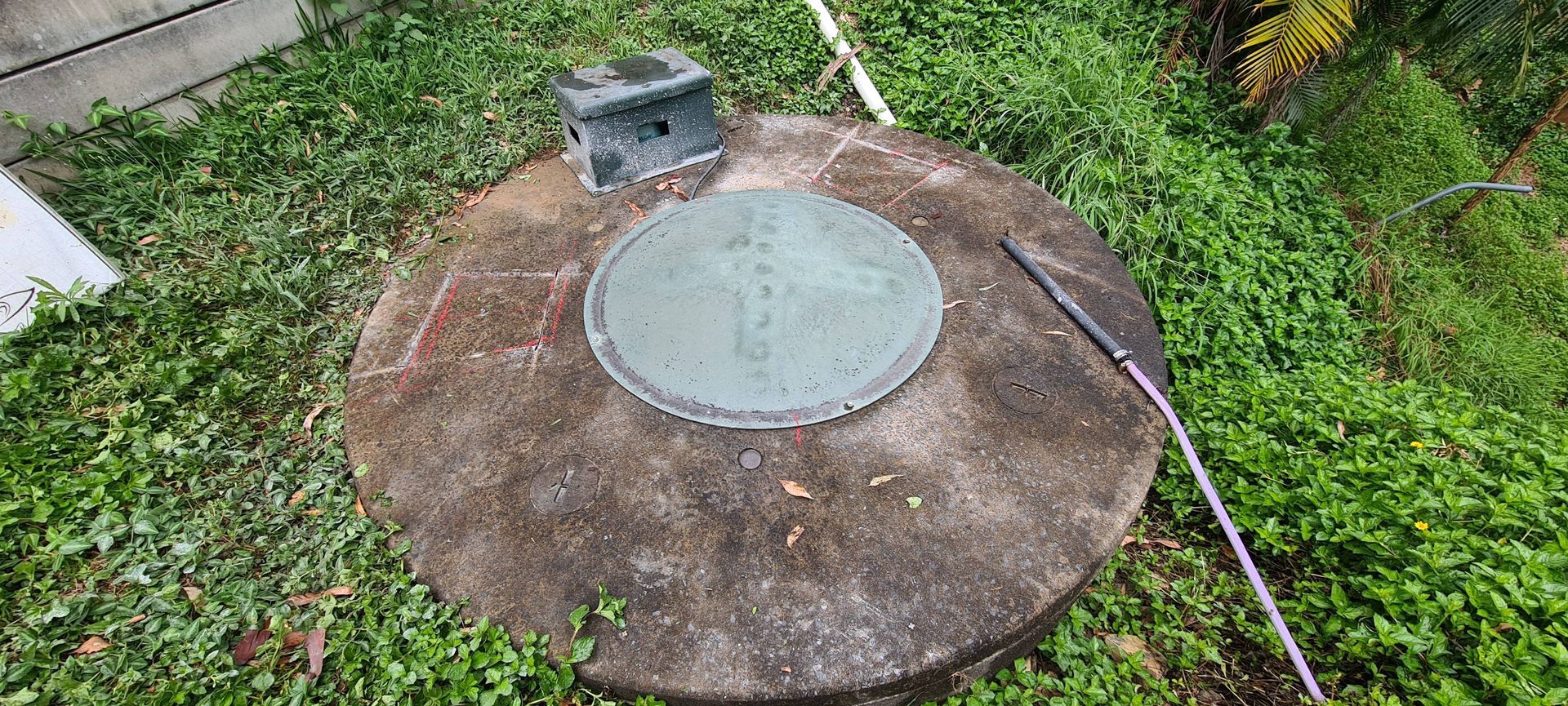 Concrete well with a circular cover, surrounded by green grass. A rectangular box sits on top — Raptor Waste Management in Coolangatta, QLD