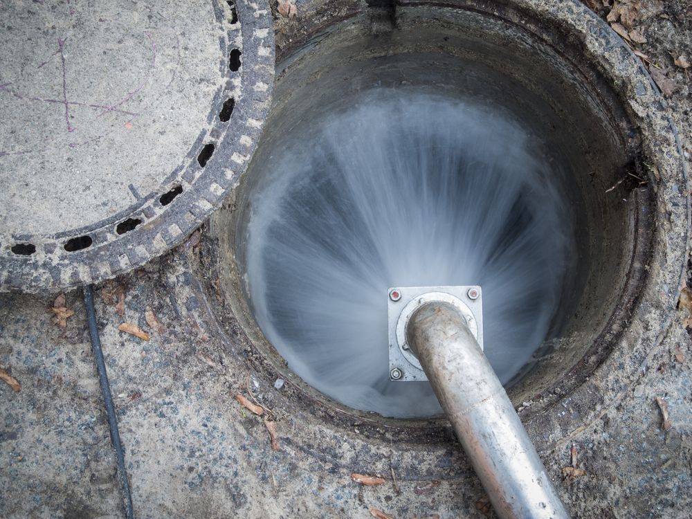 Water Spraying From a Metal Pipe Into an Open Manhole — Raptor Waste Management in Coolangatta, QLD