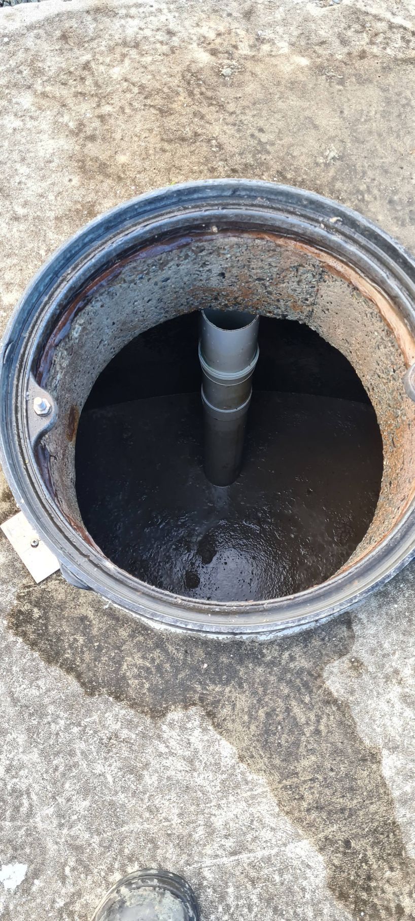 A sewer access point with dark liquid inside and a central pipe. Gray concrete surrounds — Raptor Waste Management in Coolangatta, QLD