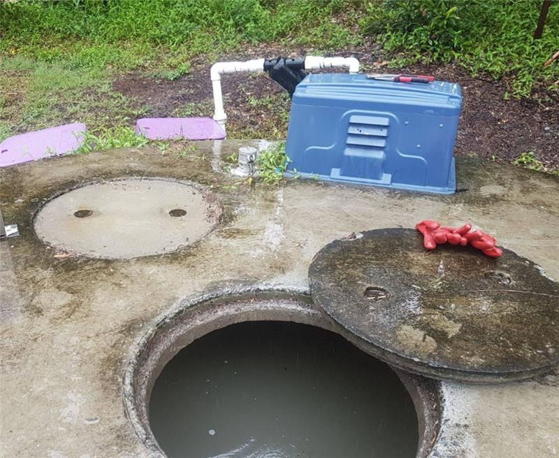 Open manhole with water, concrete surround, pipe, and blue container outdoors — Raptor Waste Management in Coolangatta, QLD
