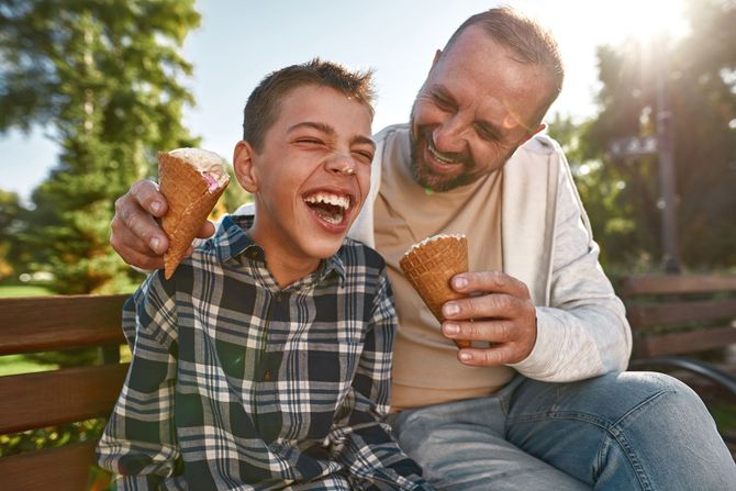 a man and a boy are sitting on a bench eating ice cream cones