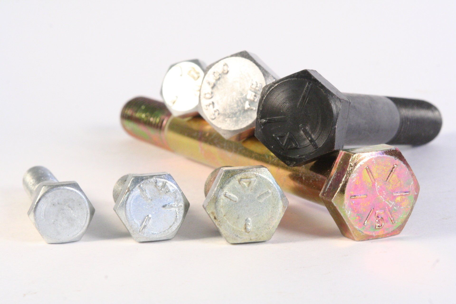 A group of bolts of different sizes and colors are sitting on top of each other on a white surface.