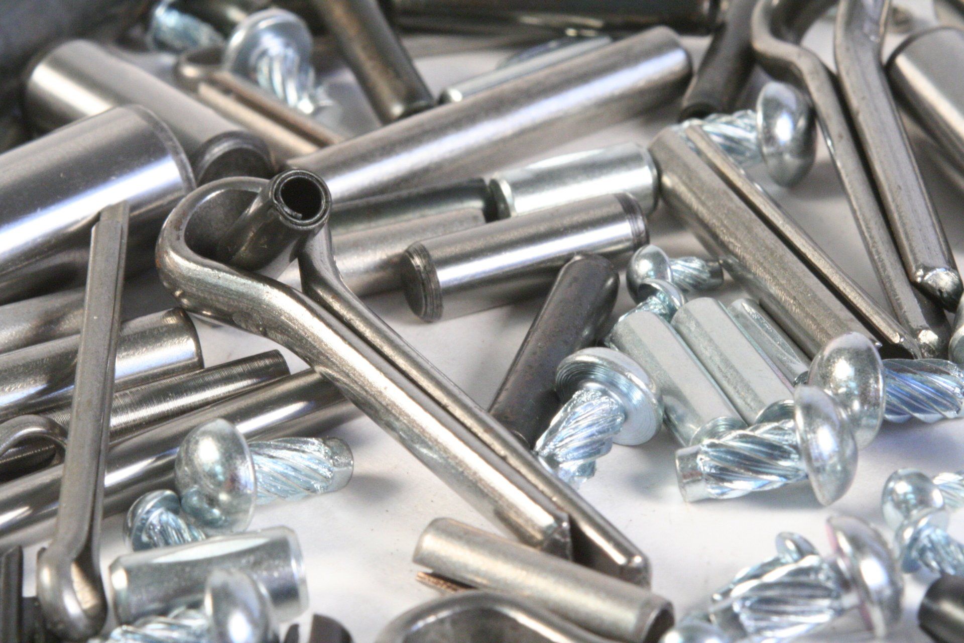 A pile of metal objects including pins and screws on a white surface.