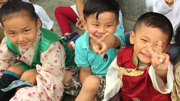 A group of children are sitting on the ground and giving peace signs.