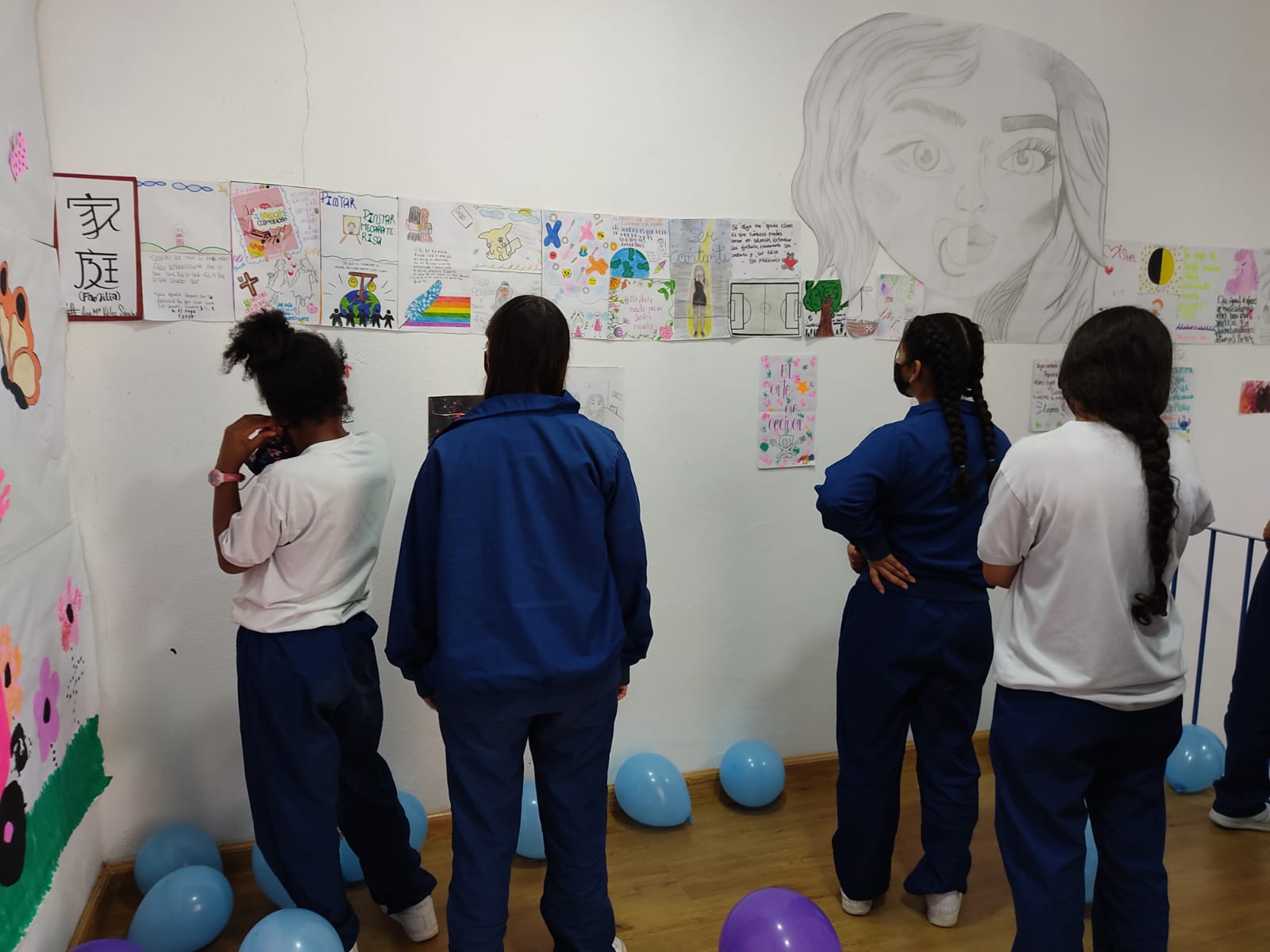 A group of girls are standing in front of a wall with drawings on it.
